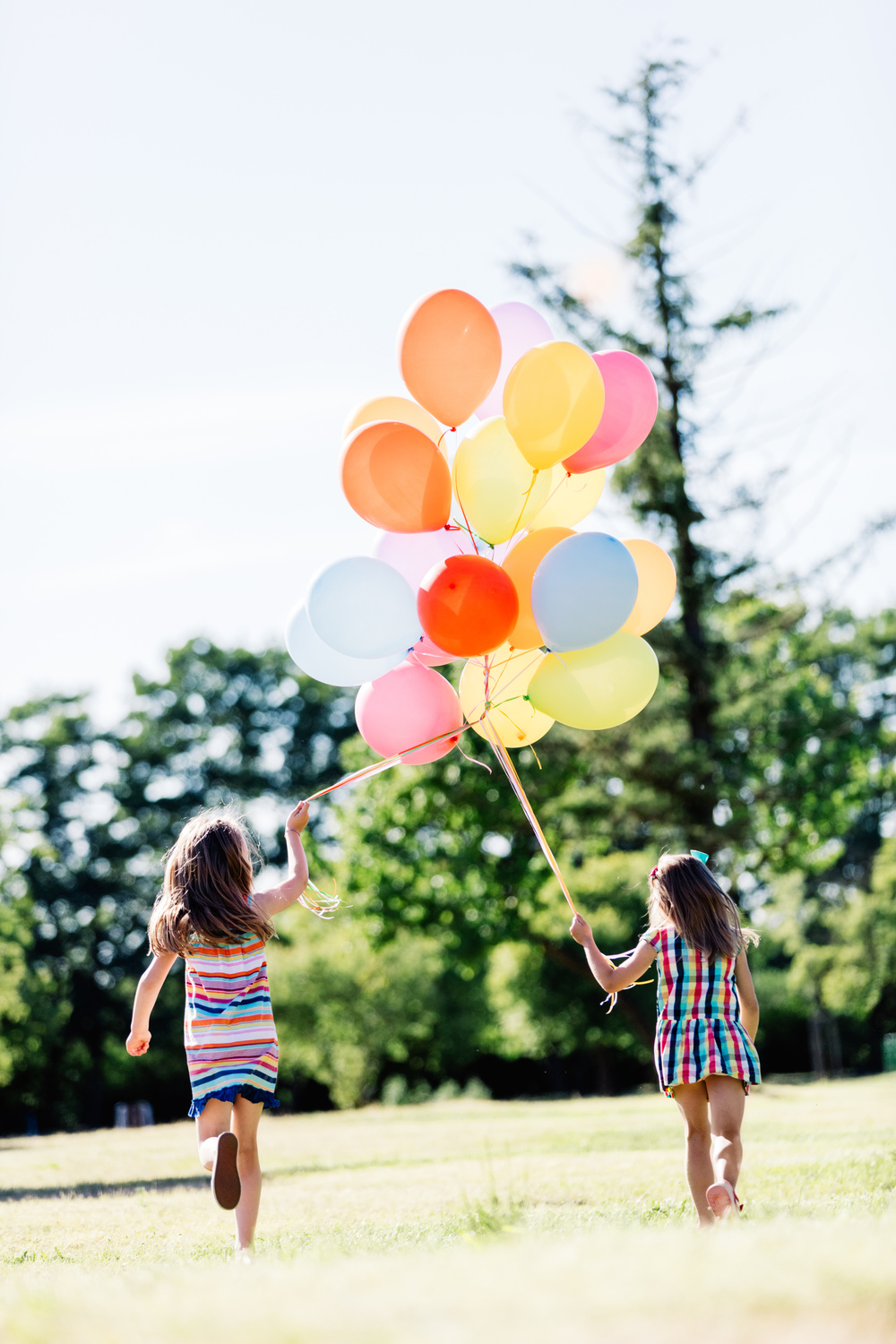 Two Little Girls Holding a Bunch of Balloons Together.